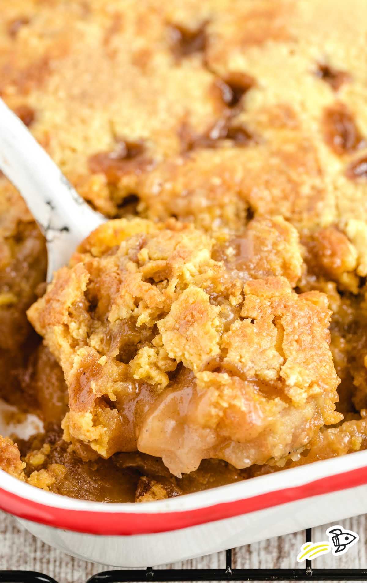 close up shot of caramel apple dump cake in a baking dish with a large spoon