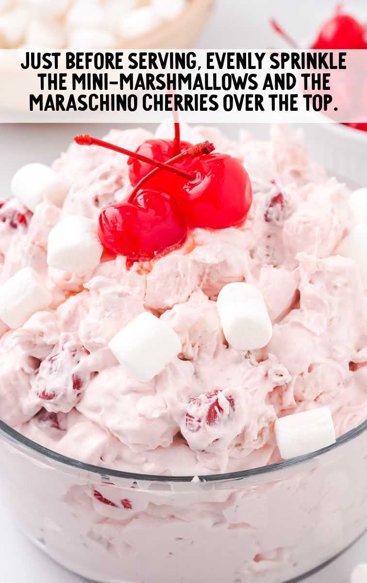 a serving bowl of cherry fluff garnished with mini marshmallows and cherries