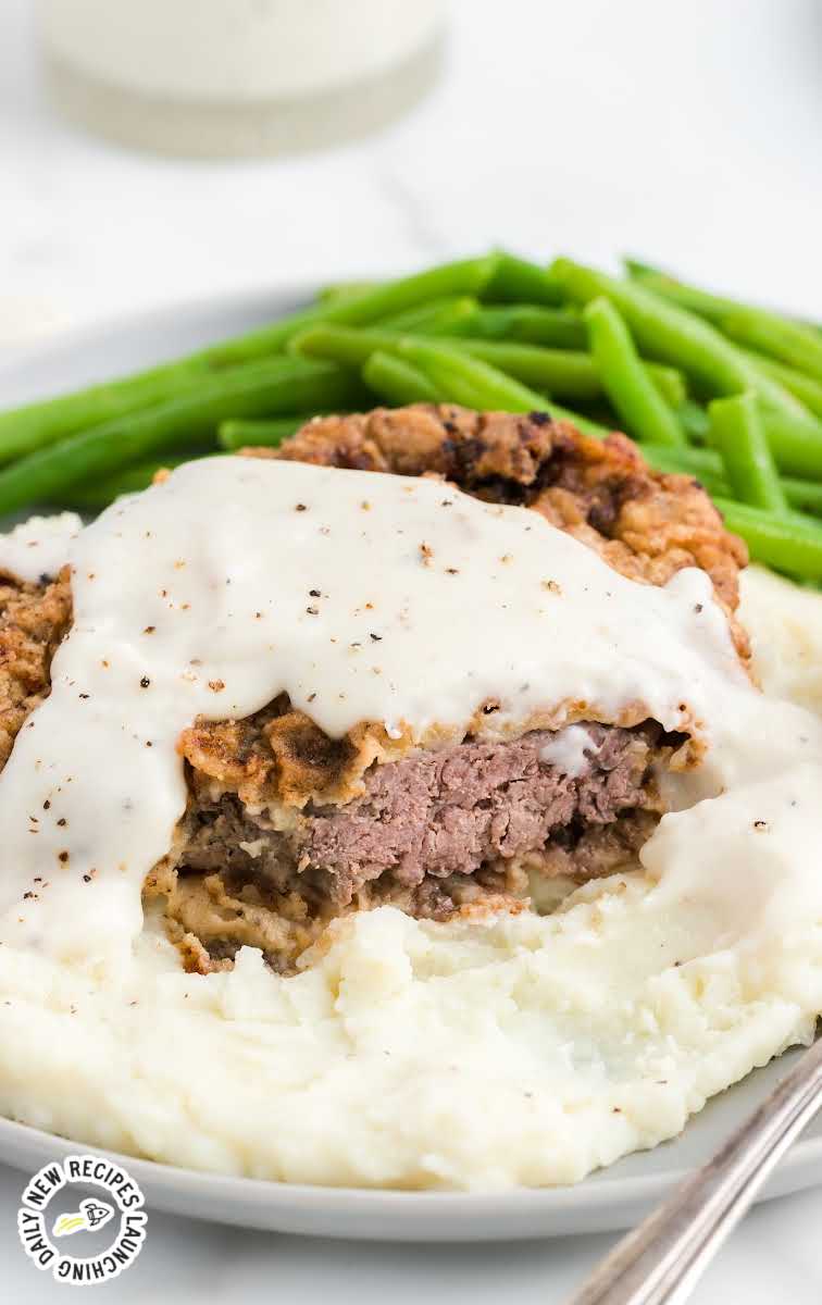 close up shot of a plate of Chicken Fried Steak with gravy served with a site of mashed potatoes and green beans