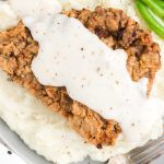 close up overhead shot of Chicken Fried Steak topped with homemade gravy and served with mashed potatoes and green beans