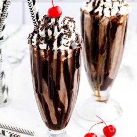close up shot of glasses of Chocolate Milkshake topped with whipped cream then garnished with Hershey bars, a cherry, chocolate sprinkles, and chocolate syrup