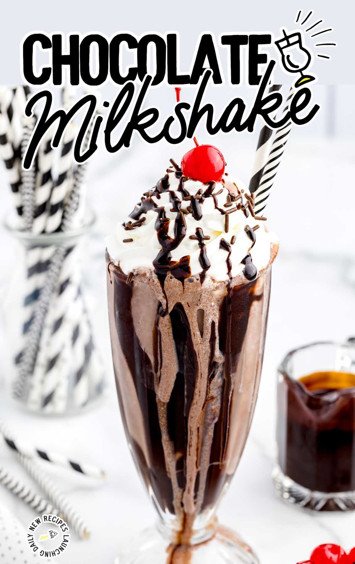 close up shot of a glass of Chocolate Milkshake topped with whipped cream then garnished with Hershey bars, a cherry, chocolate sprinkles, and chocolate syrup