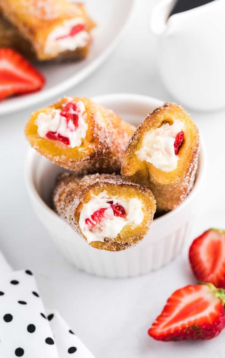 close up shot of a bowl of French Toast Roll-Ups rolled in cinnamon sugar with slices of strawberries