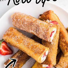 close up shot of French Toast Roll-Ups rolled in cinnamon sugar piled on a plate with slices of strawberries