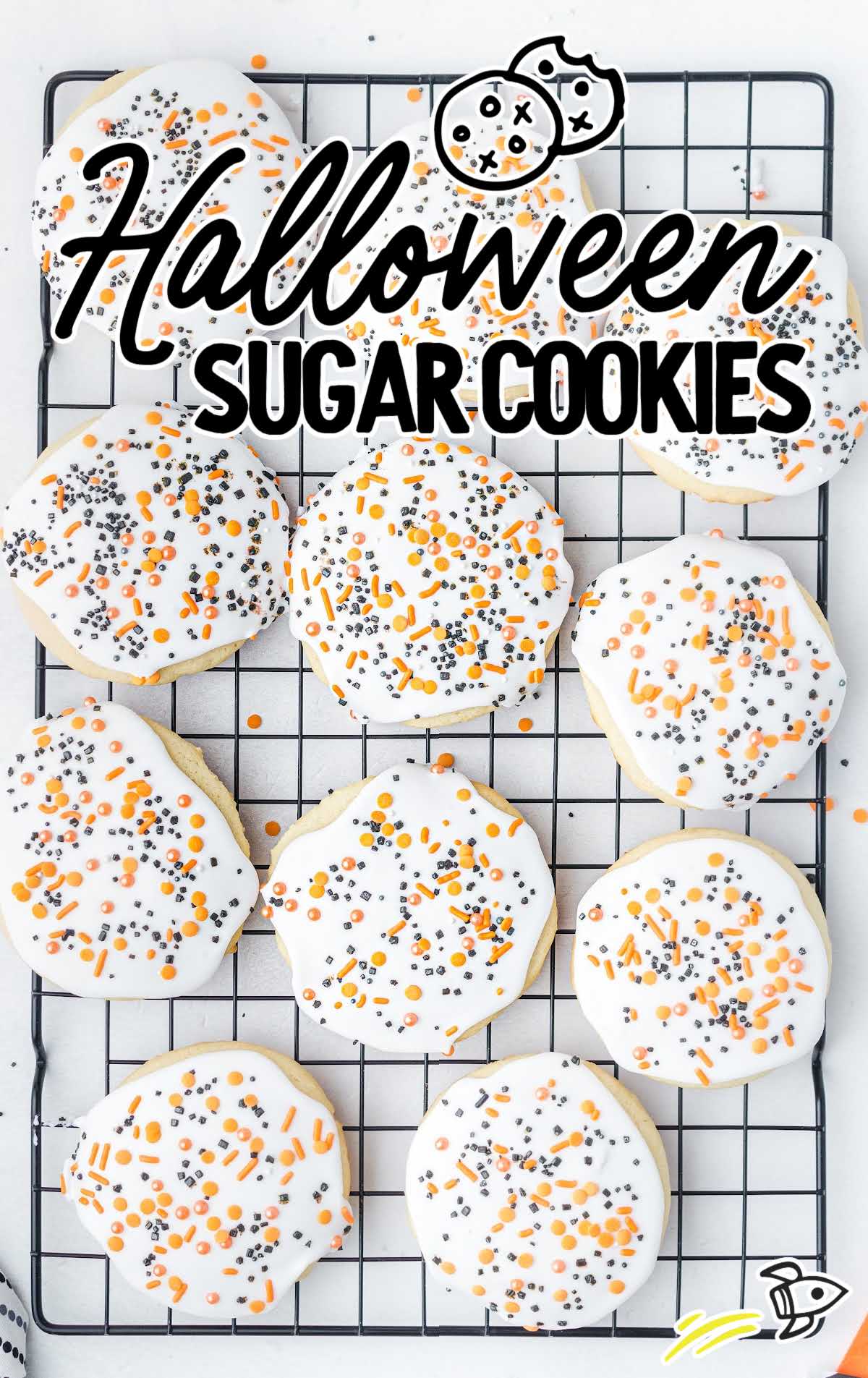 Halloween sugar cookies with white icing and orange and black sprinkles on a cooling rack