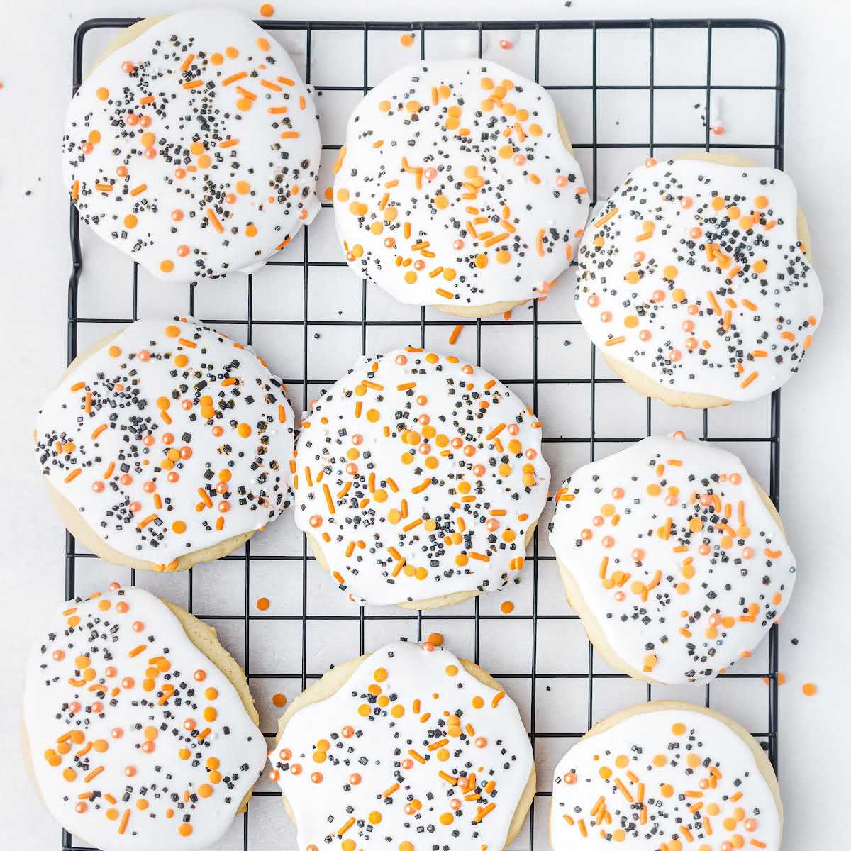 Overhead view of iced Halloween sugar cookies on a cooling rack with orange and black sprinkles