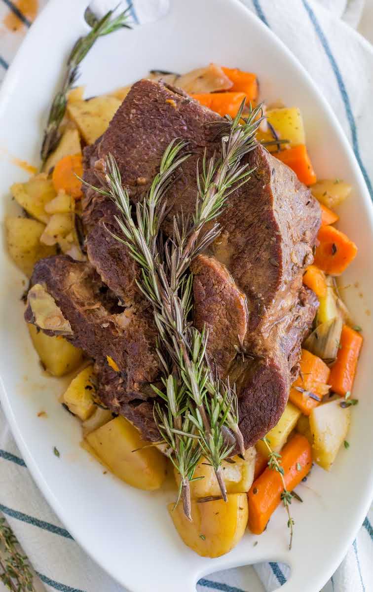 close up overhead shot of instant pot pot roast served over carrots and potatoes on a plate with a piece of thyme on top