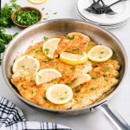 close up shot of Lemon Chicken topped with lemon slices and garnished with parsley in a skillet