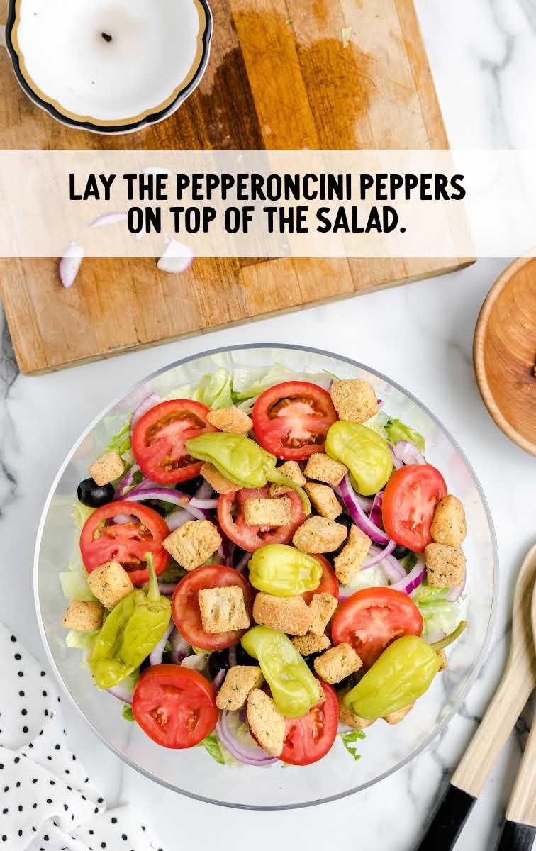 pepperoncini pepper being placed on top of a bowl of salad