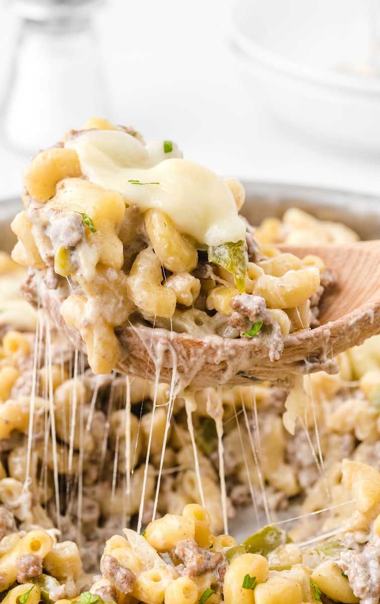 close up shot of philly Cheesesteak Pasta in a pot with a serving being picked up with a large wooden spoon