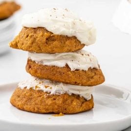close up shot of Pumpkin Cookies with Cream Cheese Frosting sprinkled with cinnamon stacked on top of each other on a plate