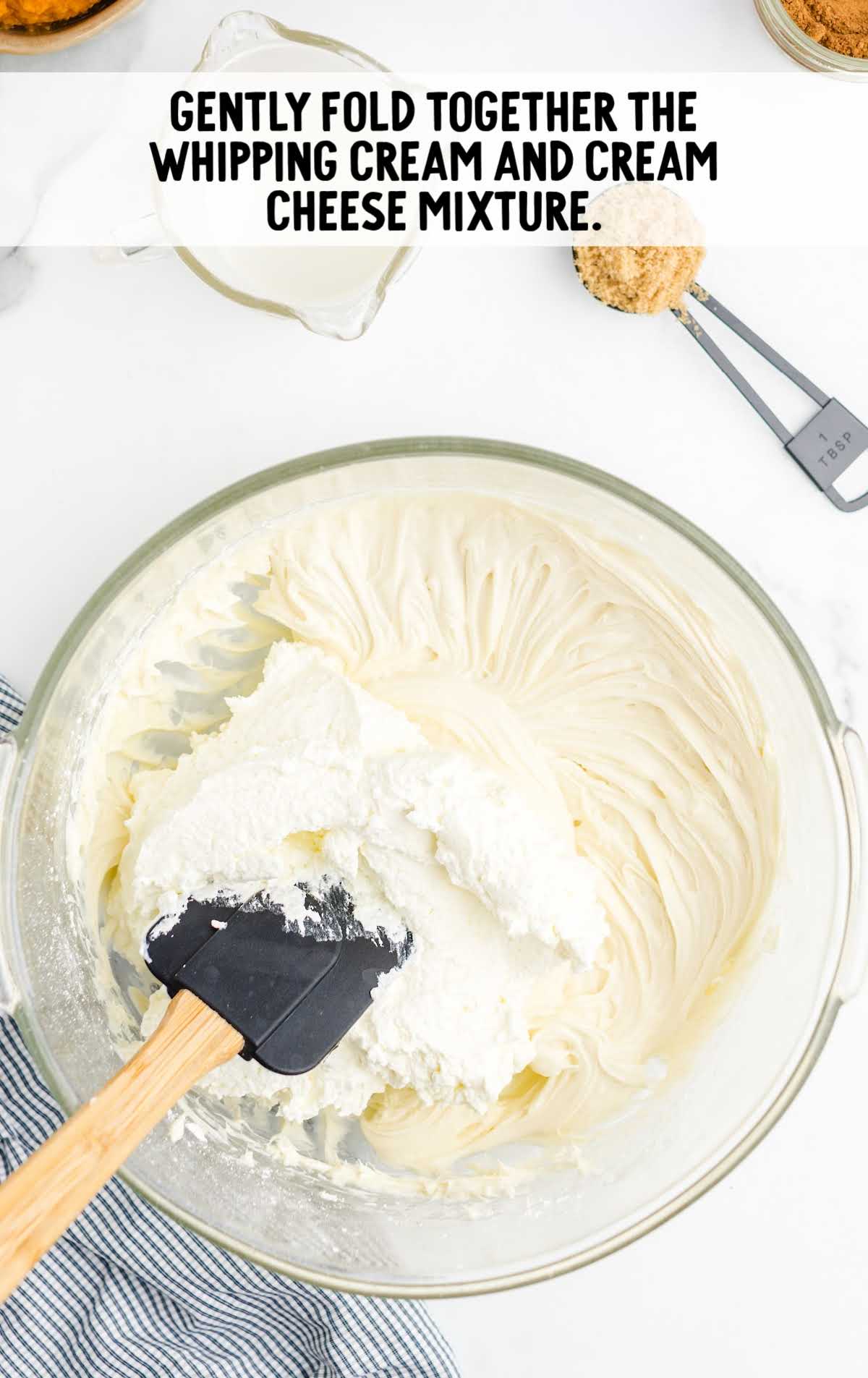 whipped cream and cream cheese mixture being folded together in a bowl