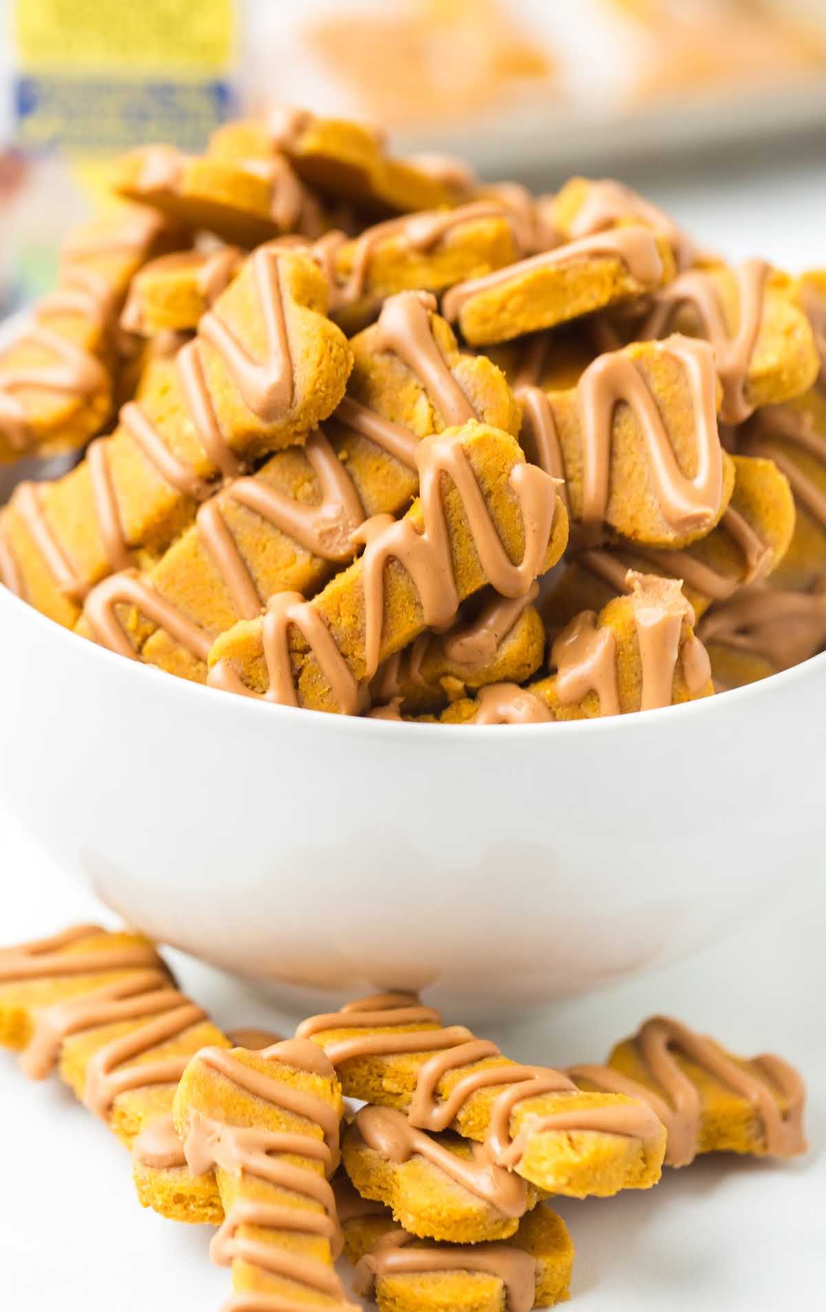 White bowl filled with pumpkin dog treats shaped like bones and topped with a peanut butter drizzle.