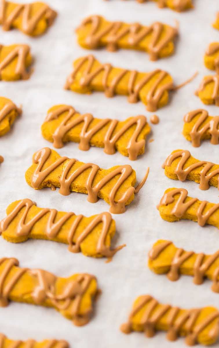 close up shot of Pumpkin Dog Treats drizzled with peanut butter on a parchment paper