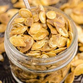 close up shot of a bunch of Roasted Pumpkin Seeds in a mason jar with a spoon on a baking sheet