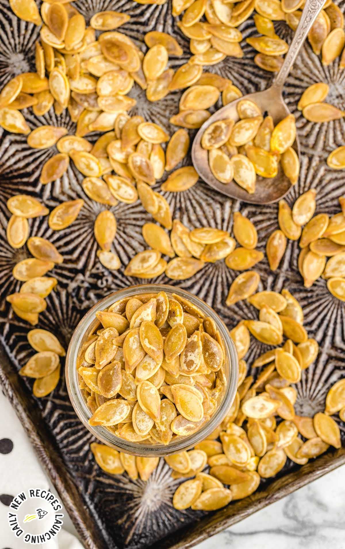 close up shot of a bunch of Roasted Pumpkin Seeds in a mason jar with a spoon on a baking sheet