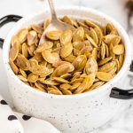 close up shot of a bunch of Roasted Pumpkin Seeds in a bowl with a spoon