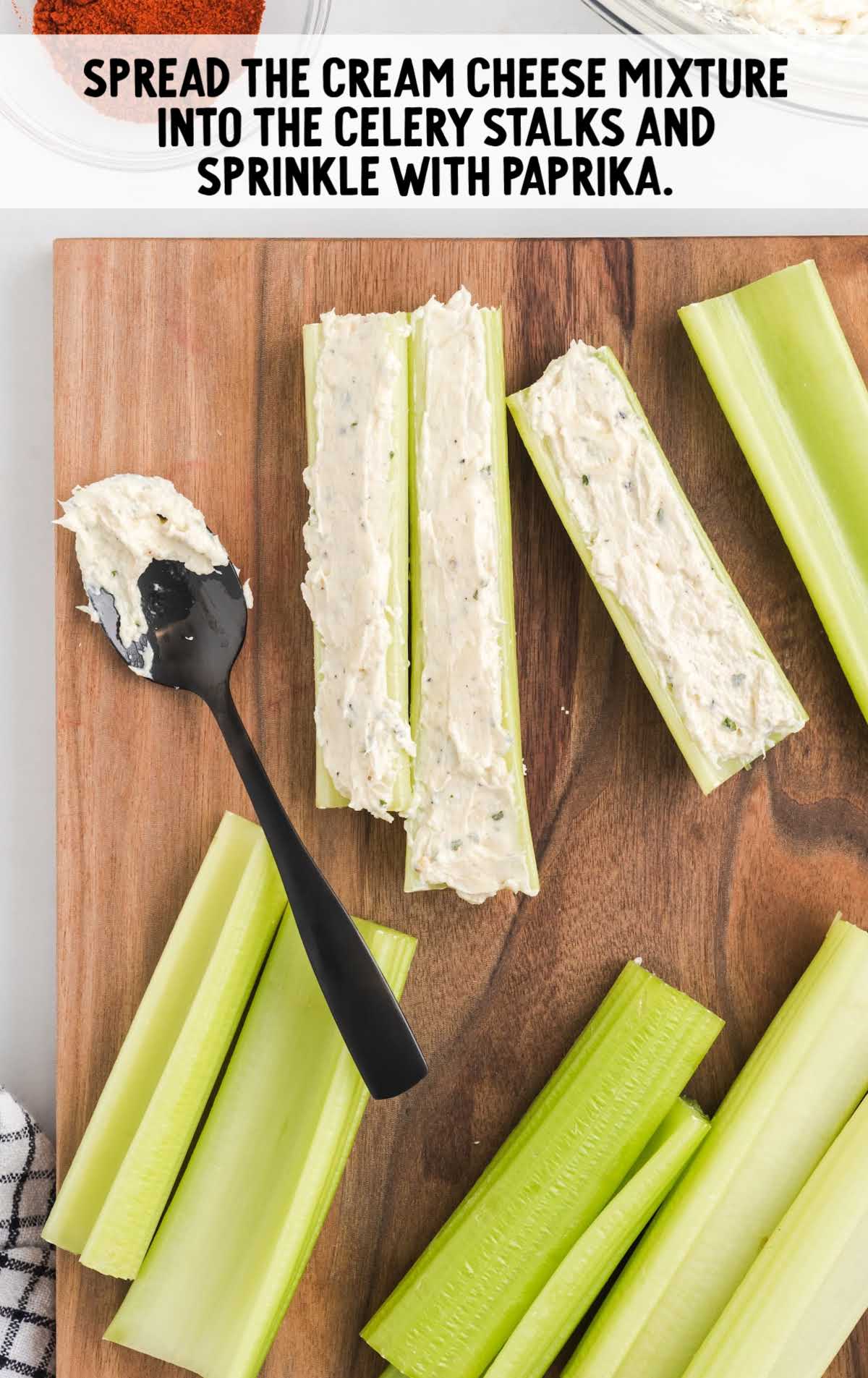 celery being stuffed with cream cheese mixture on a wooden board