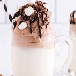 close up shot of a glass of Whipped Hot Chocolate Recipe topped with mini marshmallows and chocolate syrup with a straw
