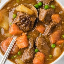 Bowl of hearty beef stew with tender beef chunks, carrots, potatoes, and peas in a rich brown broth, served with a spoon.