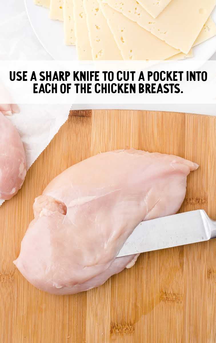 chicken cordon bleu process shot of pocket being cut into chicken breast on a wooden cutting board