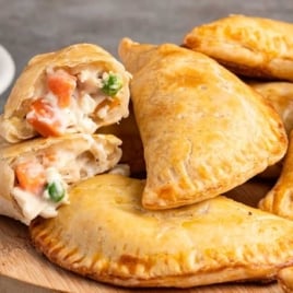 Chicken pot pie hand pies stacked on a round board with flaky crust and creamy vegetable filling inside