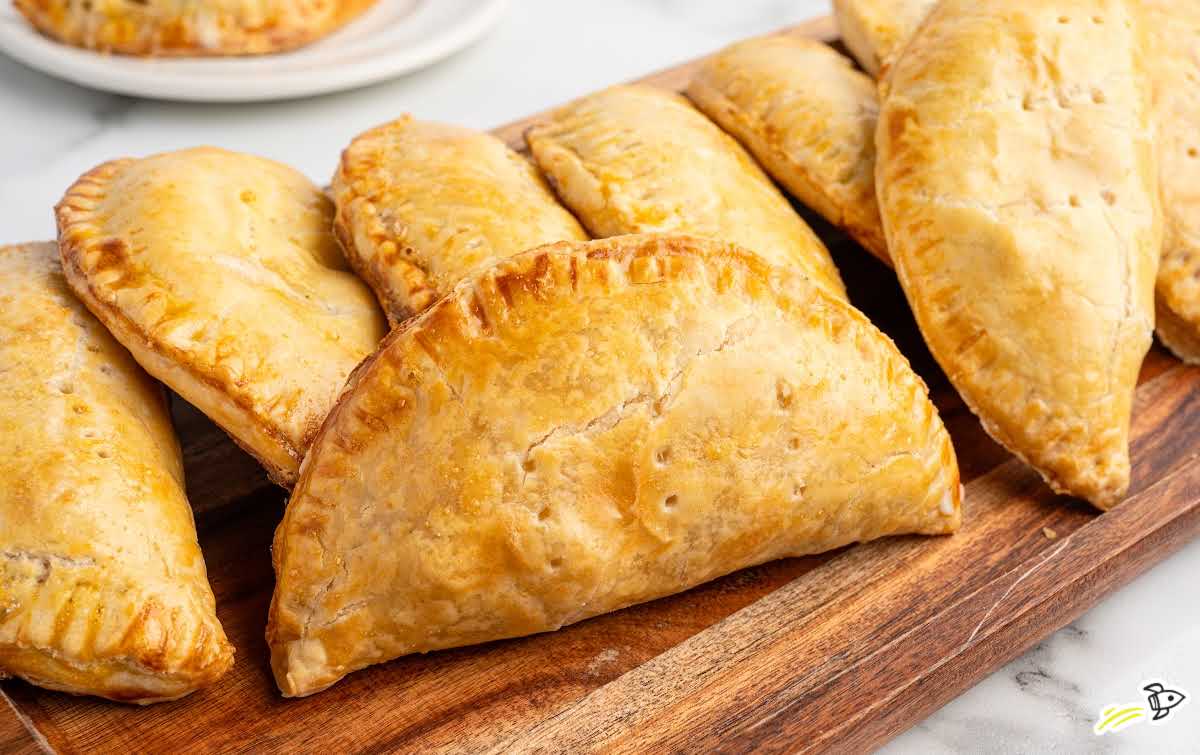 Baked chicken hand pies with fork-crimped edges arranged on a wooden serving board