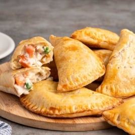 Homemade chicken hand pies with flaky golden crust and creamy chicken, peas, and carrots filling on a wooden board