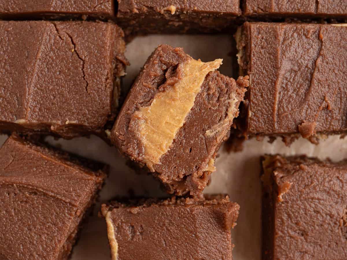 Squares of Chocolate Peanut Butter Fudge with a creamy peanut butter layer in the middle, one piece turned to show the thick peanut butter filling. The fudge pieces are arranged on a sheet of parchment paper, perfectly capturing this irresistible Chocolate Peanut Butter Fudge recipe.