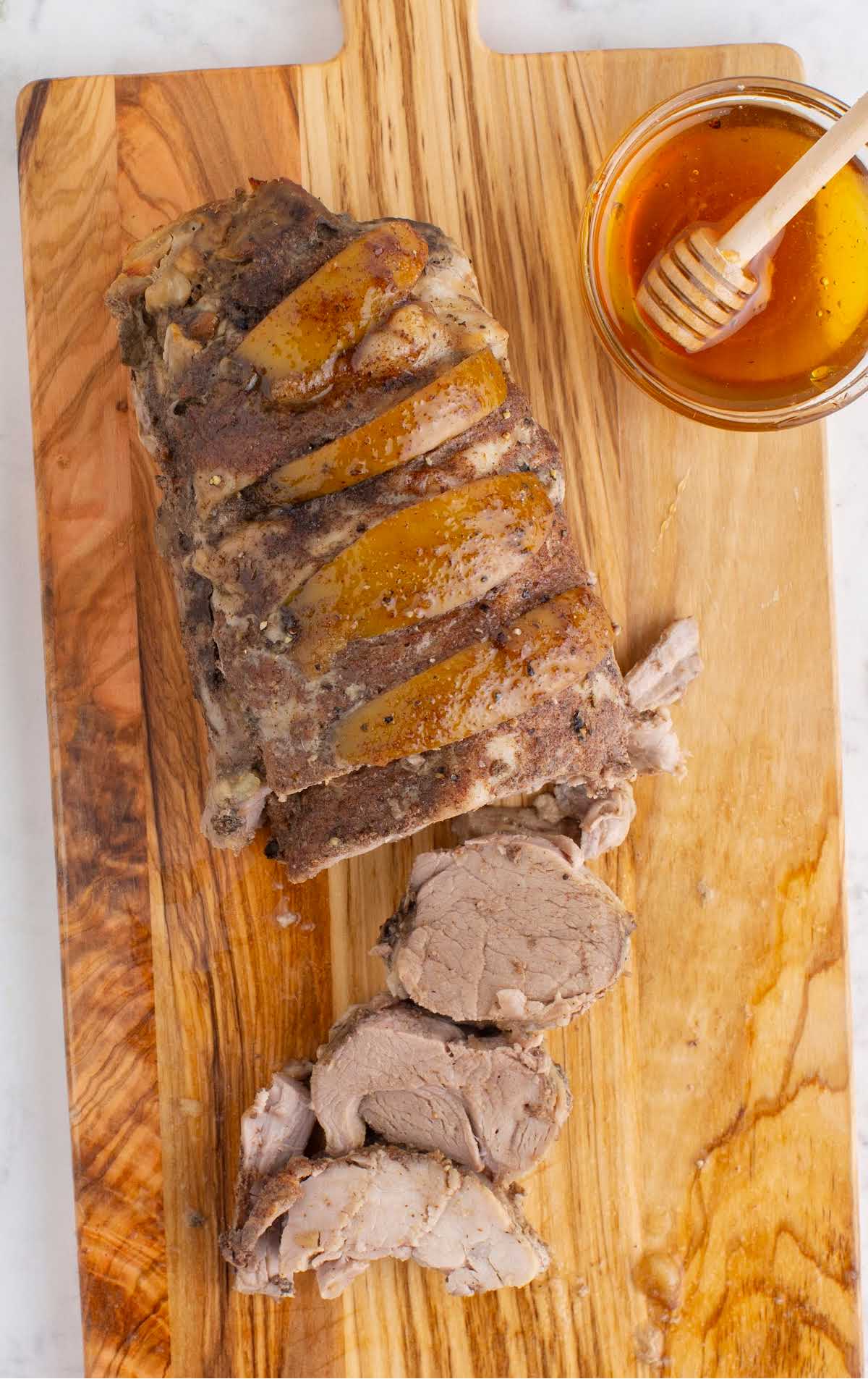 pork tenderloin sliced on a wooden board with a bowl of honey