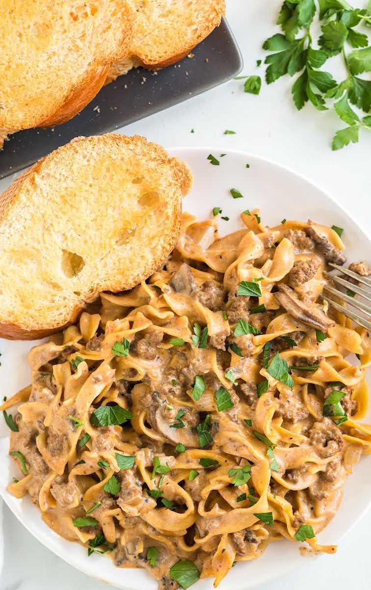 close up overhead shot of a serving of Ground Beef Stroganoff topped with parsley and served with a piece of bread