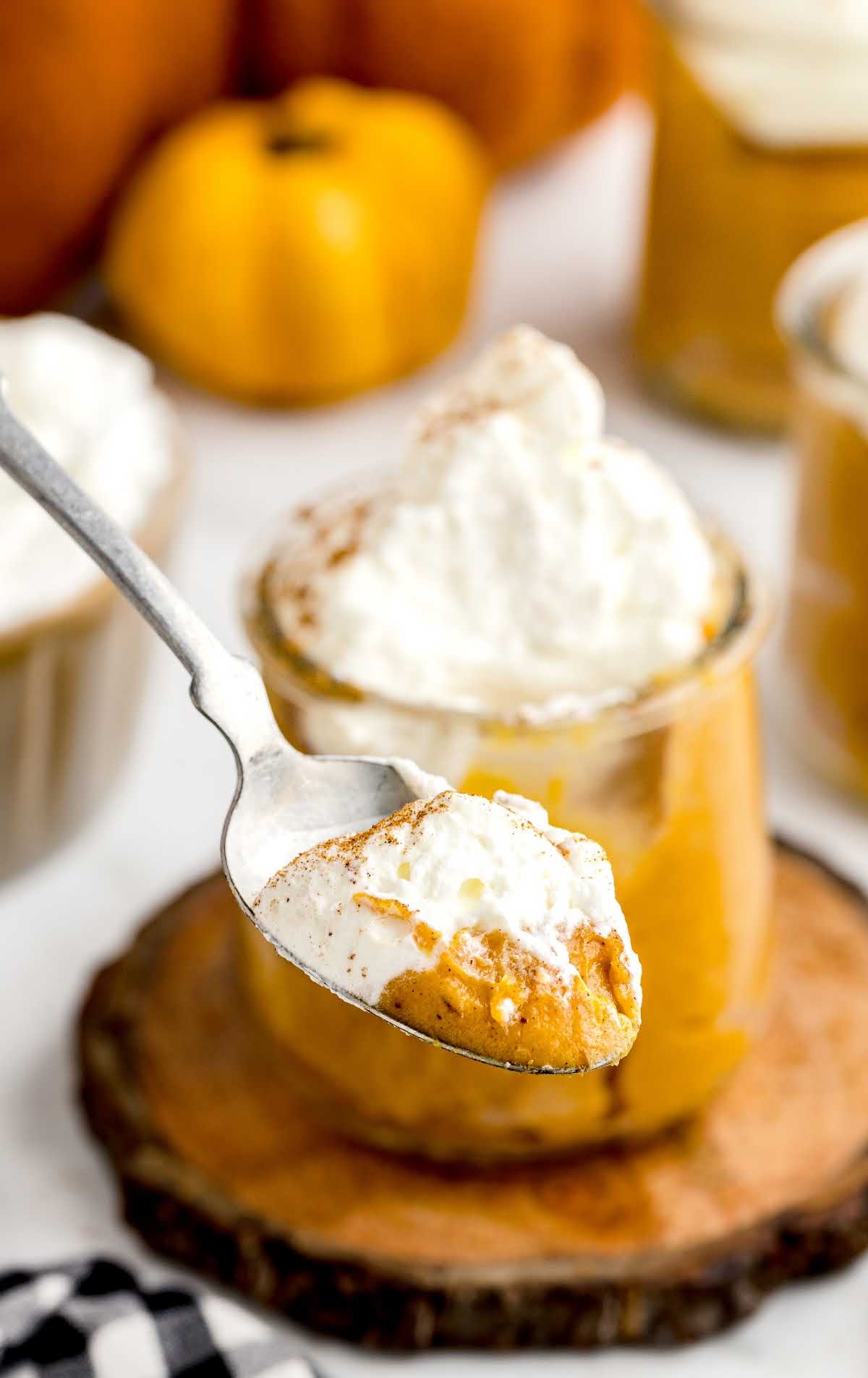 close up shot of a cup of Pumpkin Pudding topped with whipped cream and pumpkin spice with a spoon