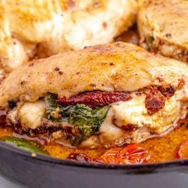 close up shot of sun dried tomato stuffed chicken in a skillet with tomato slices and spinach