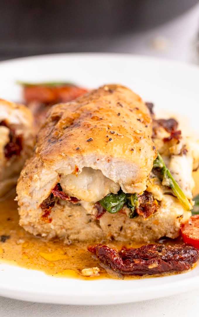 close up shot of a piece of sun dried tomato stuffed chicken on a plate with tomato slices and spinach