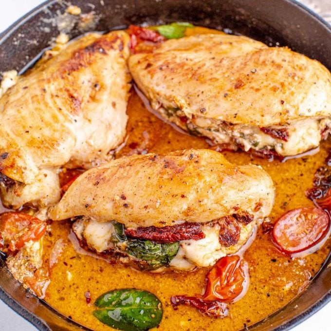 close up shot of sun dried tomato stuffed chicken in a skillet with tomato slices and spinach