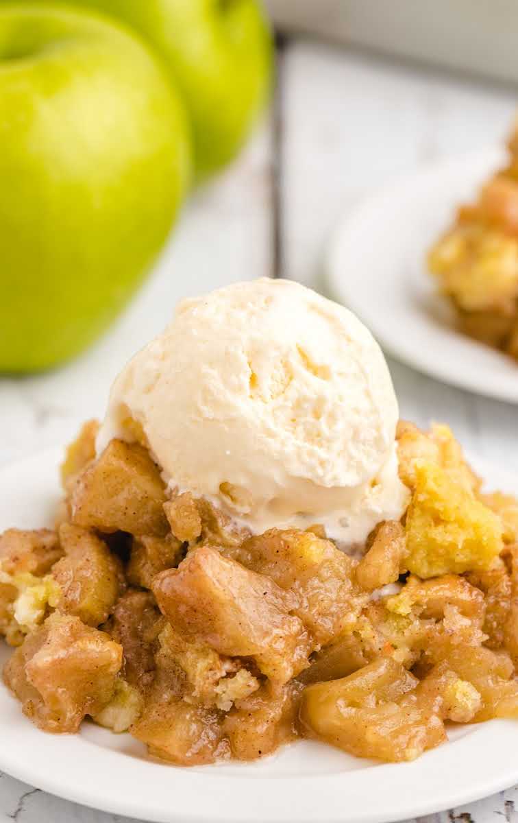 close up shot of a serving of apple dump cake topped with vanilla ice cream on a plate