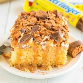 close up shot of a slice of Butterfinger Cake garnished with butterfinger candy bits on a plate