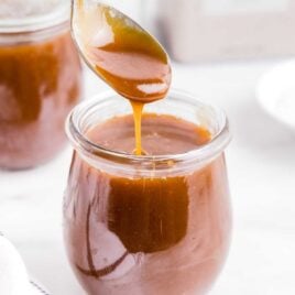 close up shot of Caramel Sauce in a jar with a spoonful of sauce being scooped out of the jar