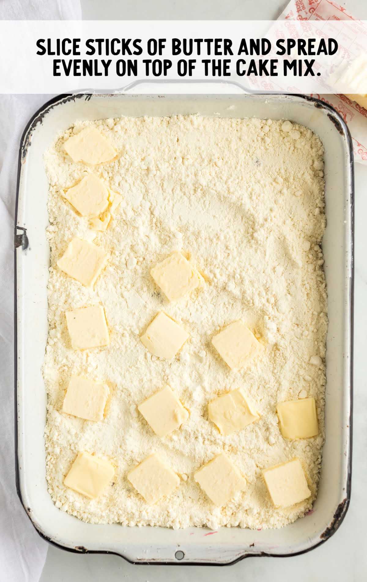 slices of butter being spread over cake mix in a baking dish
