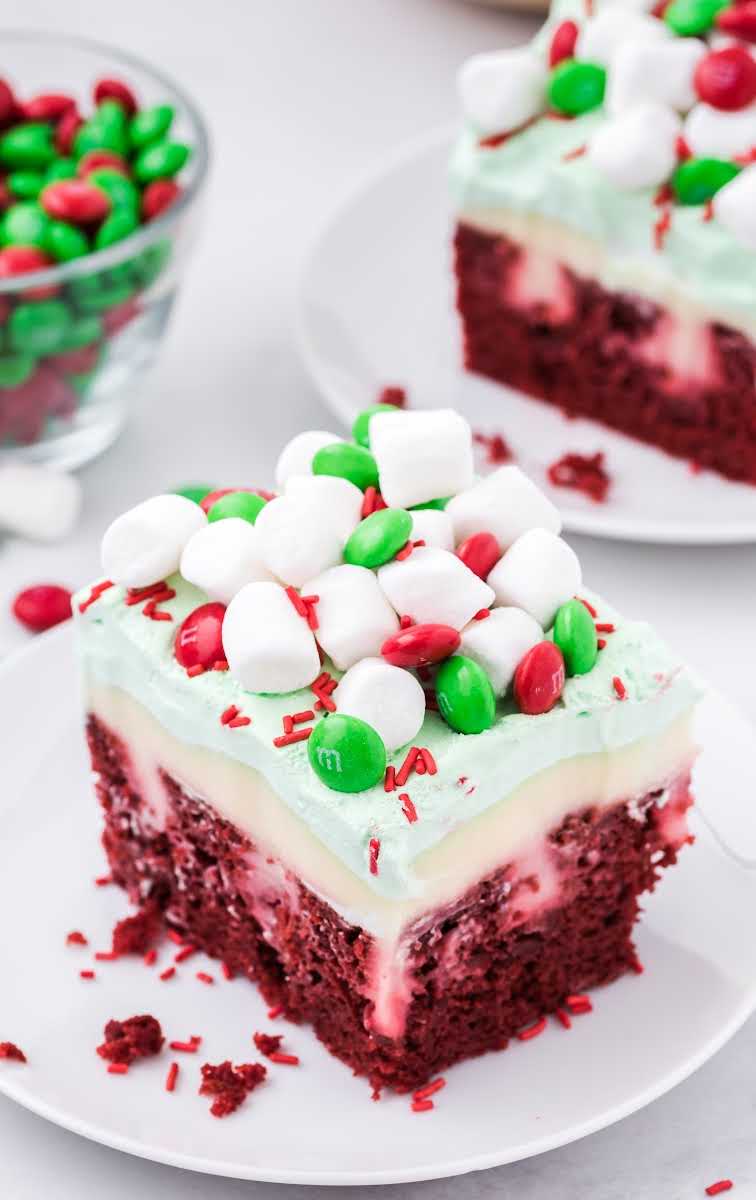 close up shot of a slice of Christmas Red Velvet Poke Cake topped with mini marshmallows and m&ms on a plate