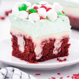 close up shot of a slice of Christmas Red Velvet Poke Cake topped with mini marshmallows and m&ms on a plate