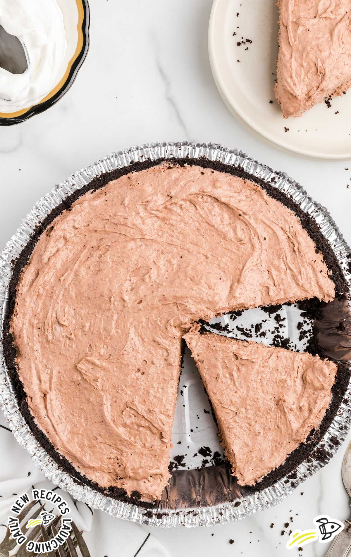 Overhead view of a chocolate cool whip pie in a foil pie pan with one slice removed and placed on a plate.