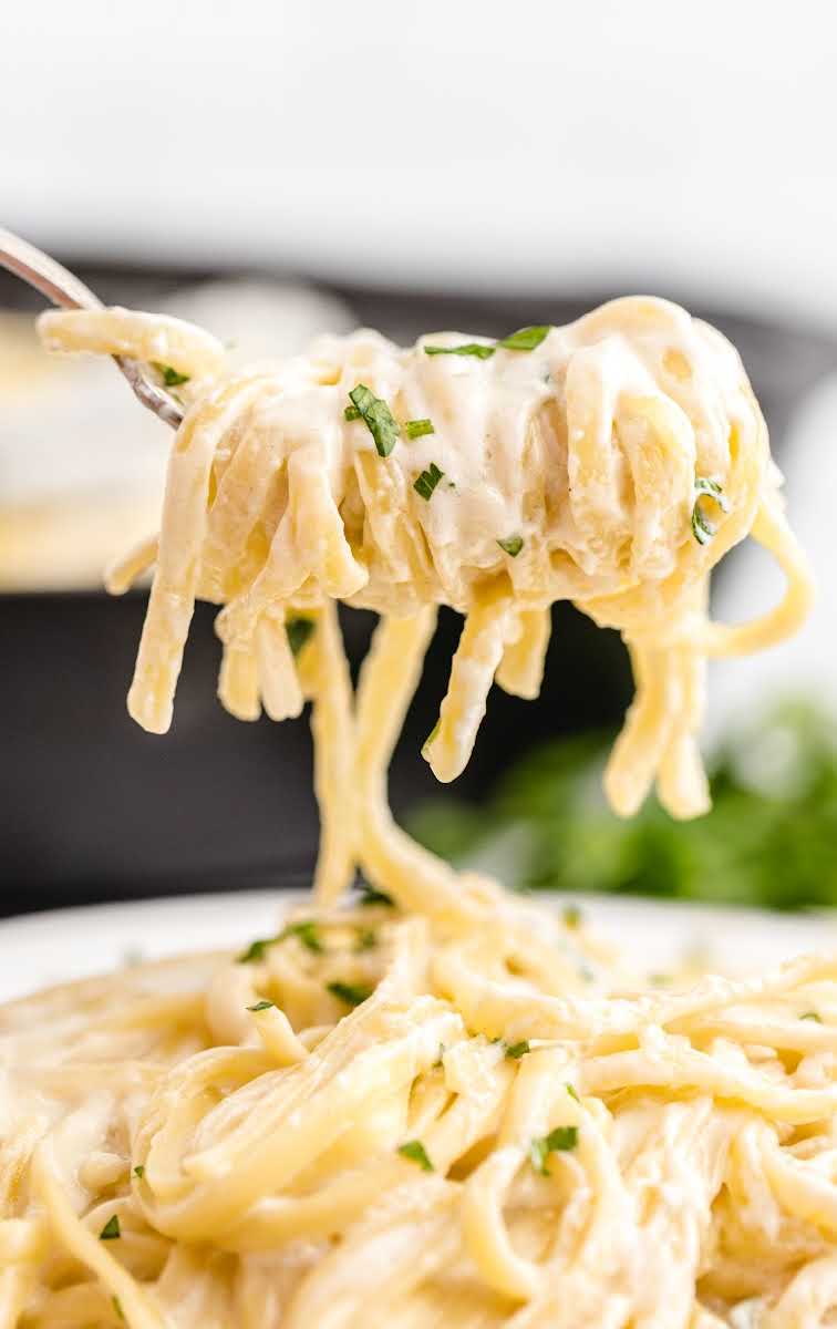 close up overhead shot of a serving of Copycat Olive Garden Alfredo Sauce with pasta and garnished with parsley in a bowl with a fork