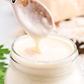 close up shot of a jar of Copycat Olive Garden Alfredo Sauce with the sauce being scooped out with a spoon