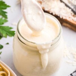 close up shot of a jar of Copycat Olive Garden Alfredo Sauce with the sauce being scooped out with a spoon
