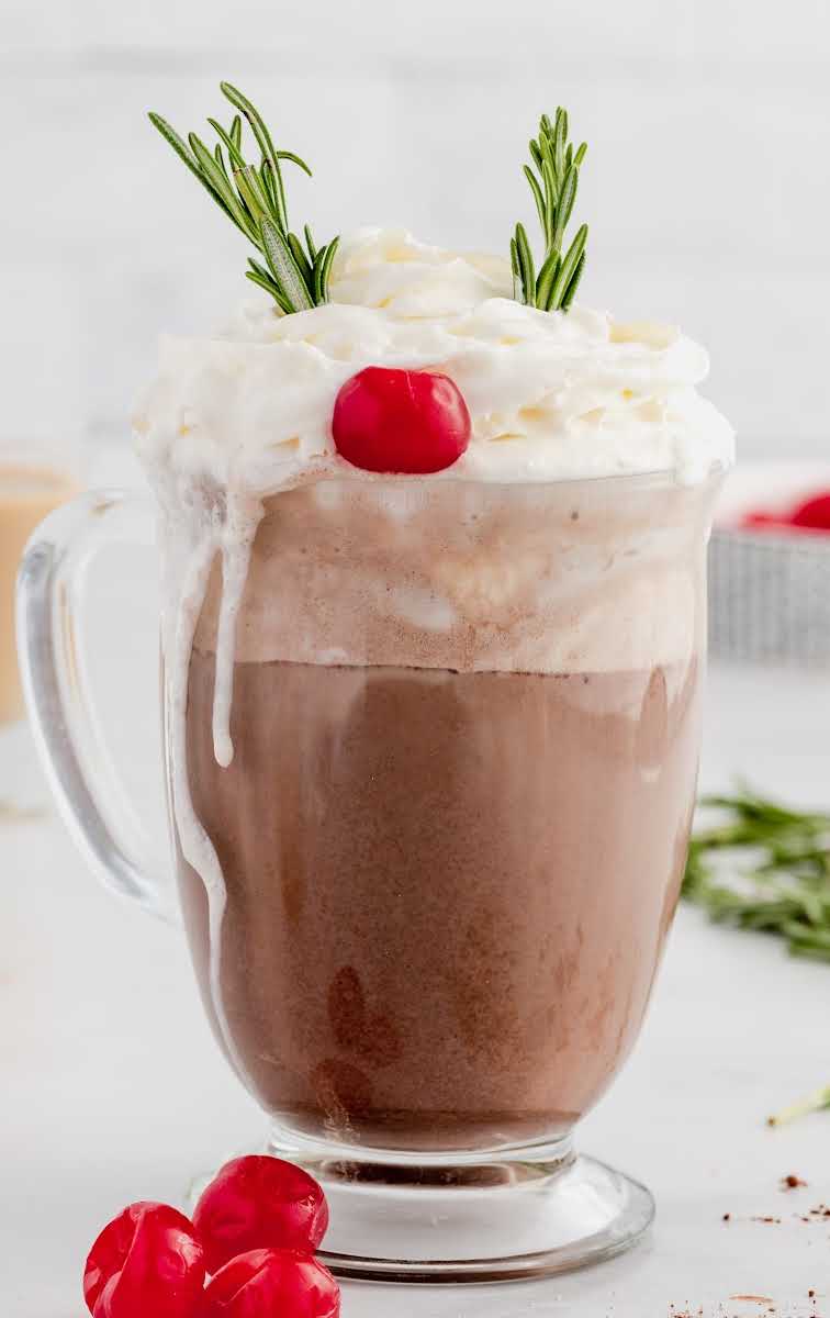 close up shot of a glass of drunken Rudolf topped with whipped cream and garnished with a maraschino cherry and rosemary