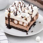close up shot of a slice of Hot Chocolate Lasagna topped with mini marshmallows and drizzled with chocolate syrup on a plate