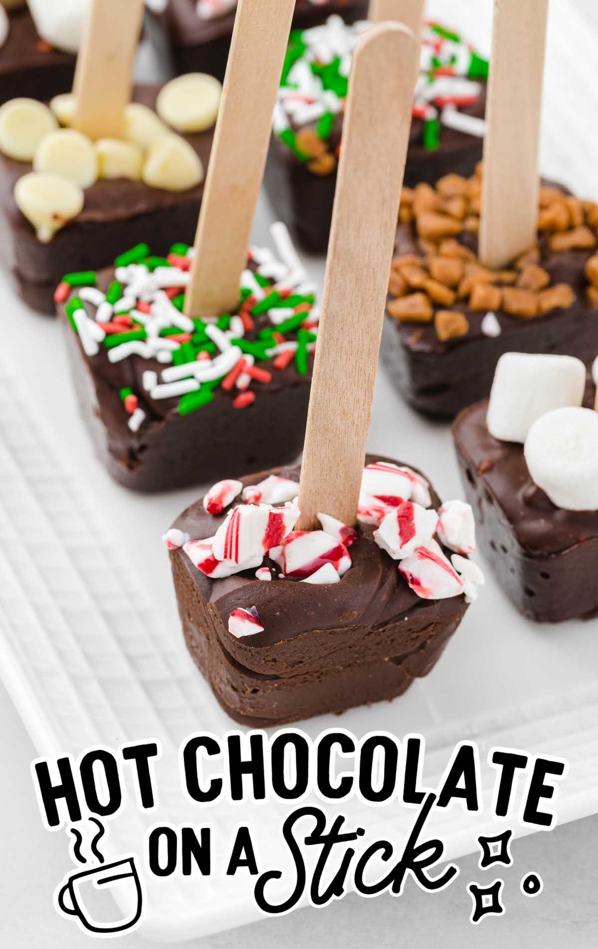 close up shot of Hot Chocolate on a stick decorated with mini marshmallows, sprinkles, crushed peppermint, and white chocolate on a serving tray 