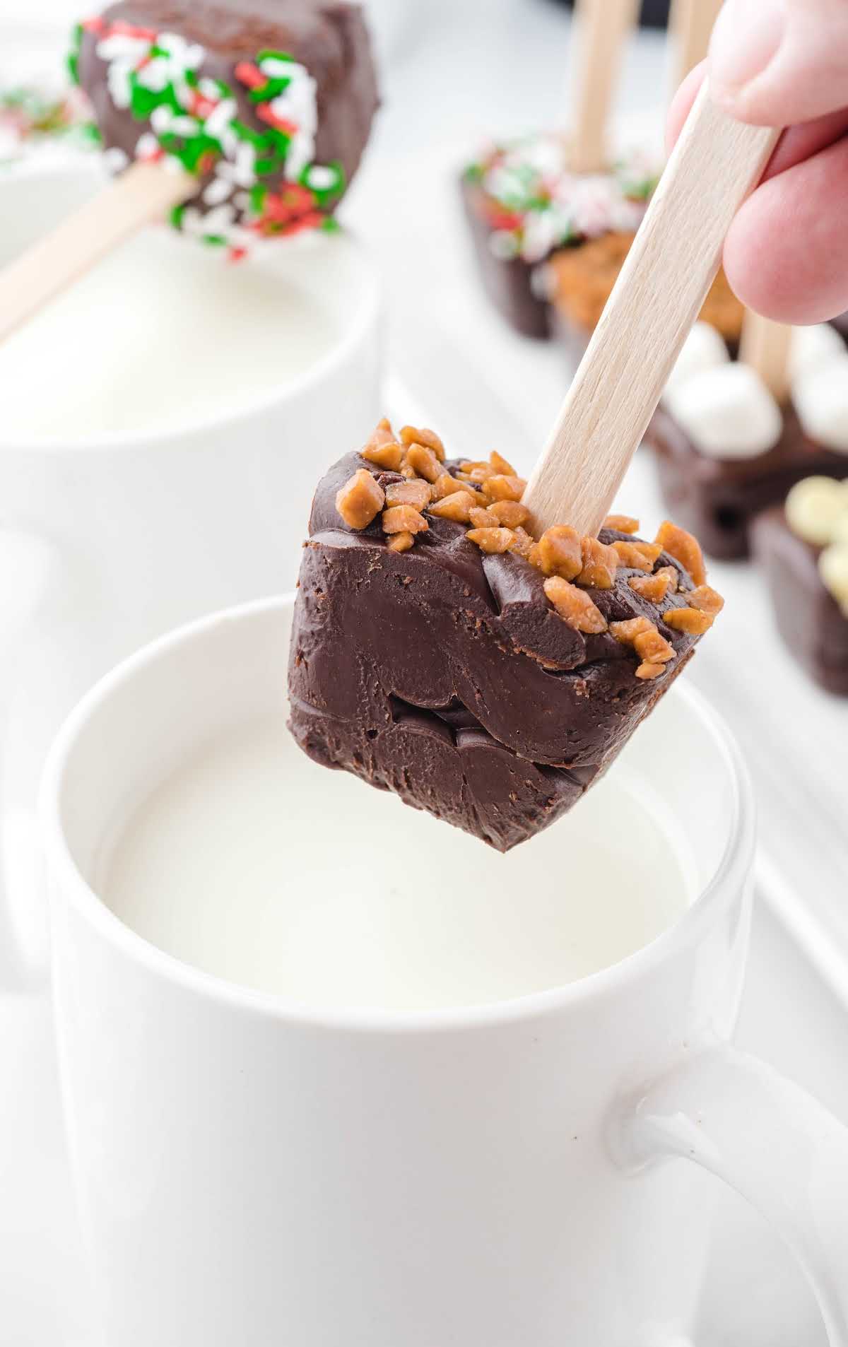 close up shot of Hot Chocolate on a stick being dipped into a coffee cup of milk 
