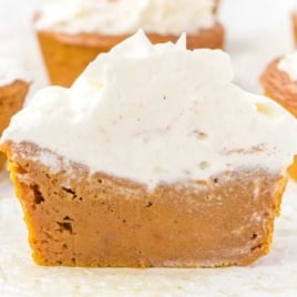 Pumpkin pie cupcake cut in half and topped with whipped cream, showing pie-like texture inside.